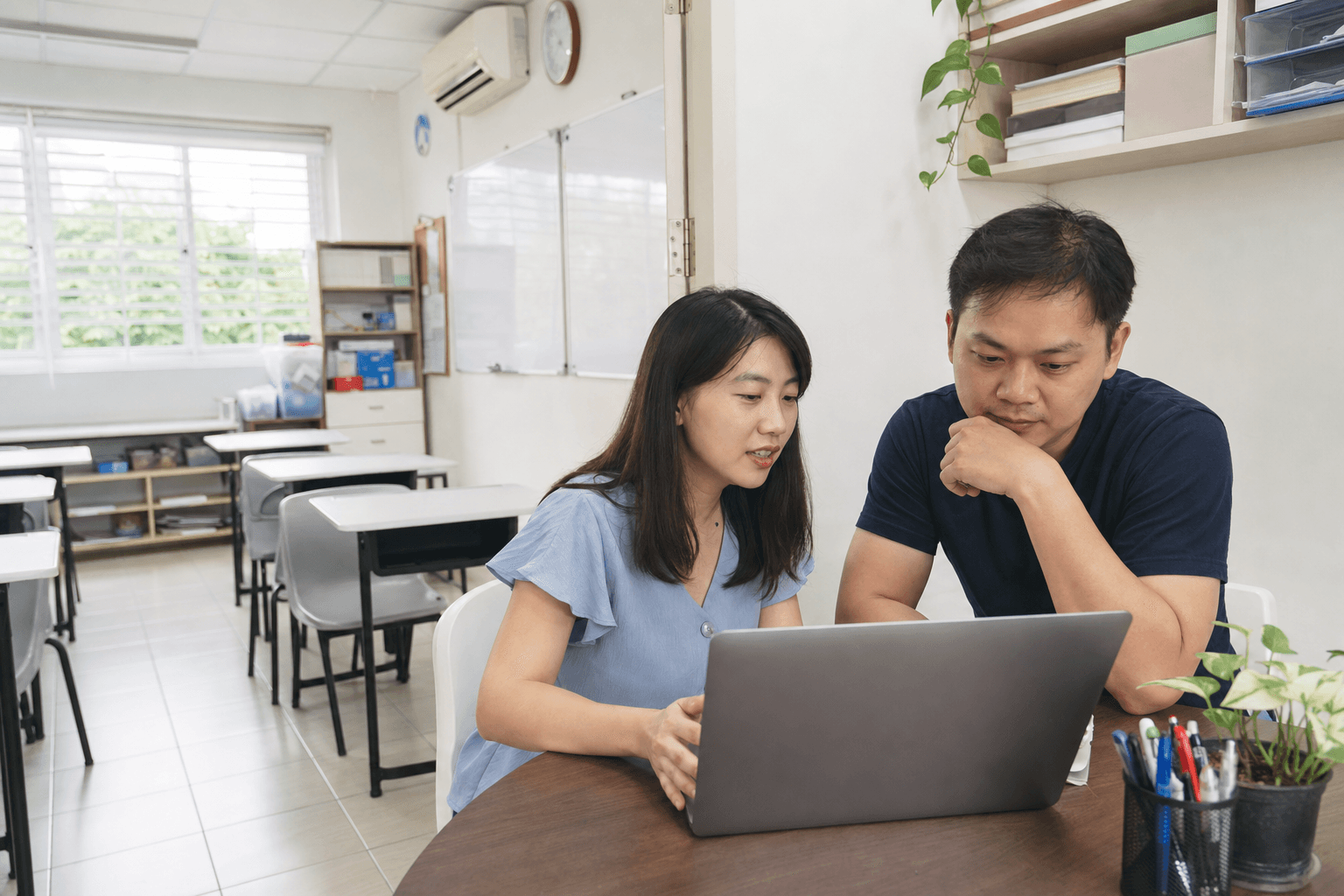 Singapore tuition centre owner and tutor reviewing the centre website in an empty classroom.